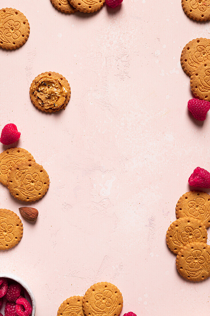 Draufsicht auf appetitliche knusprige Kekse mit Erdnussbutter mit Sesam, Himbeeren und Nüssen auf einem Tisch als abstrakter Hintergrund