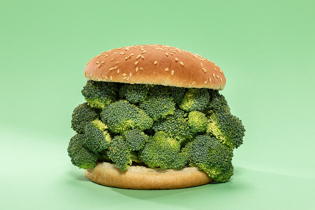 Halves of burger bun with bunch of raw broccoli served on green background during healthy lunch