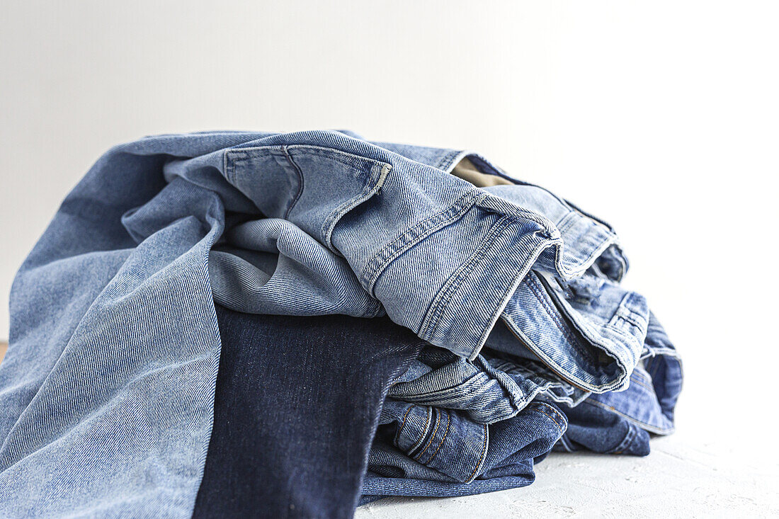 Pile of blue colored folded and crumple denim pants placed in light studio