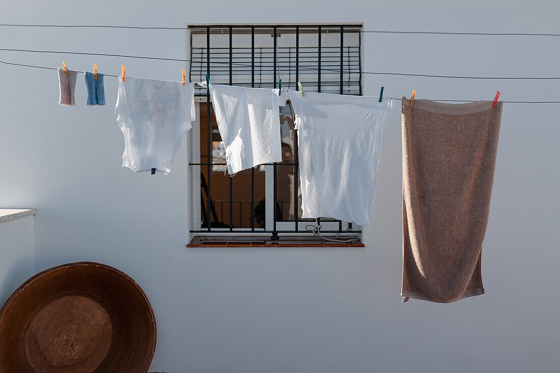 Gewaschene Wäsche hängt auf der Wäscheleine im Hof eines Landhauses mit weißen Wänden und Gitterfenster