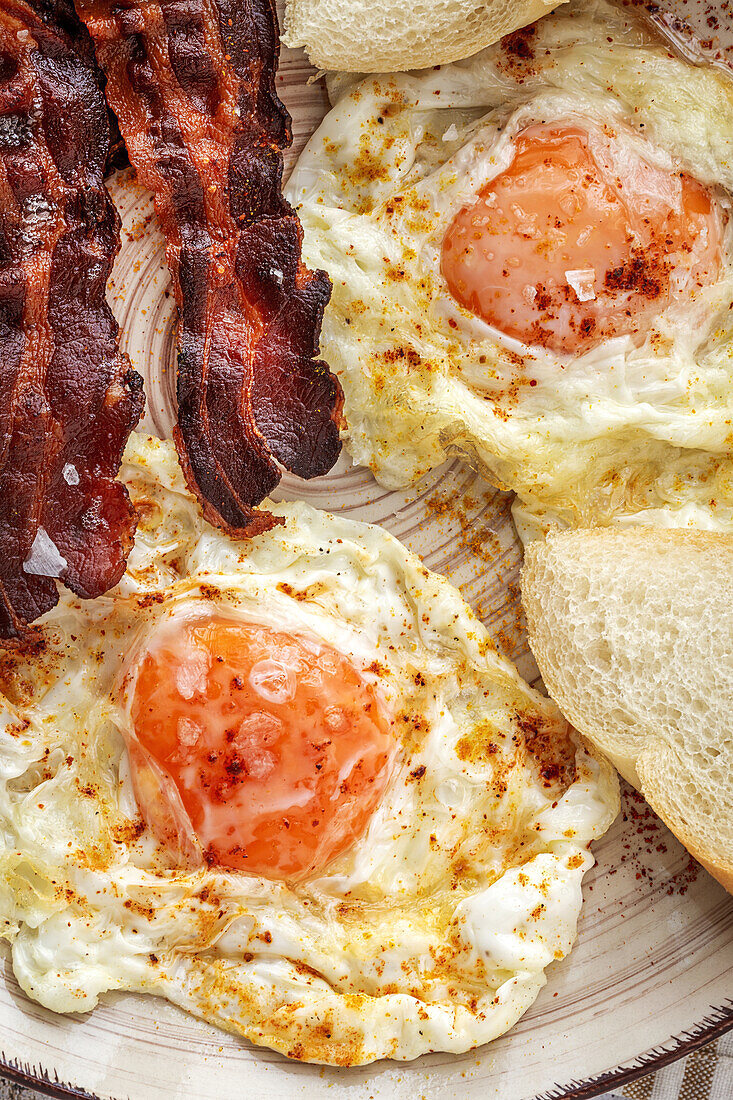 Tasty sunny side up eggs with fried bacon strips on plate