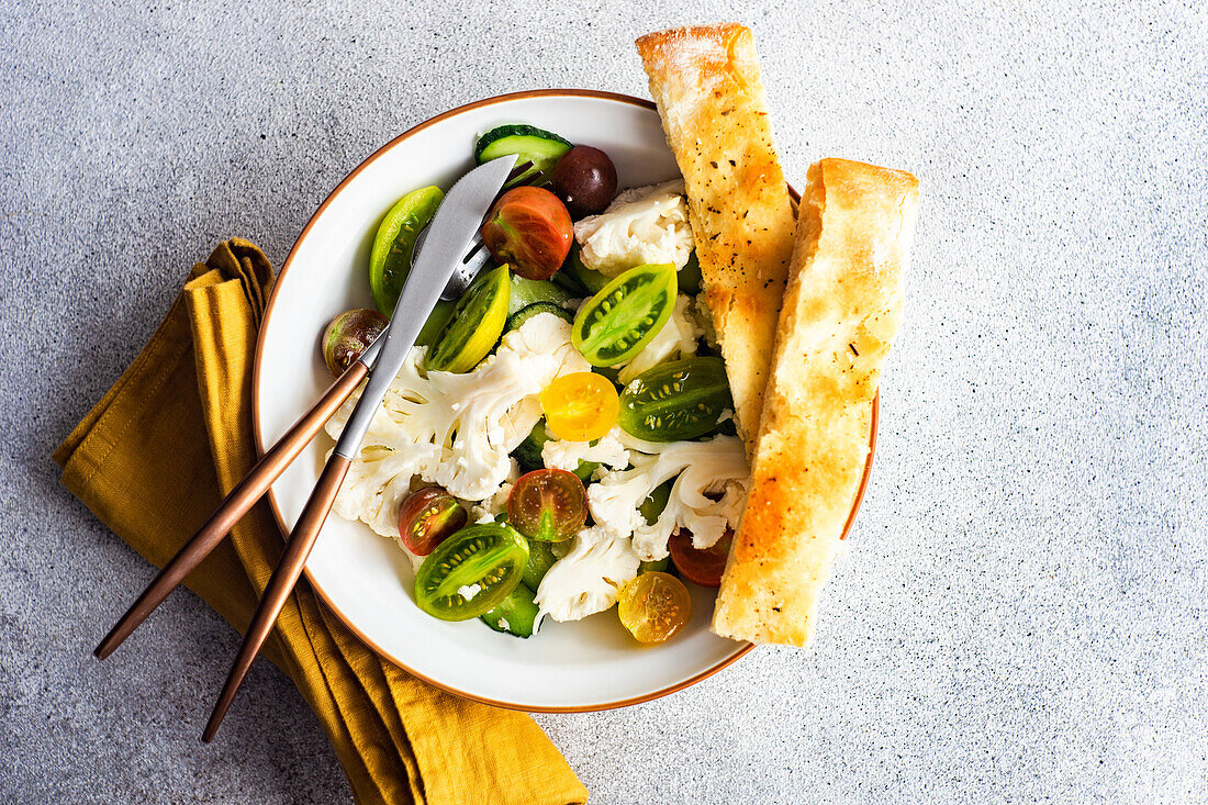 Healthy vegetable salad in the bowl and fresh baked focaccia bread served on concrete table