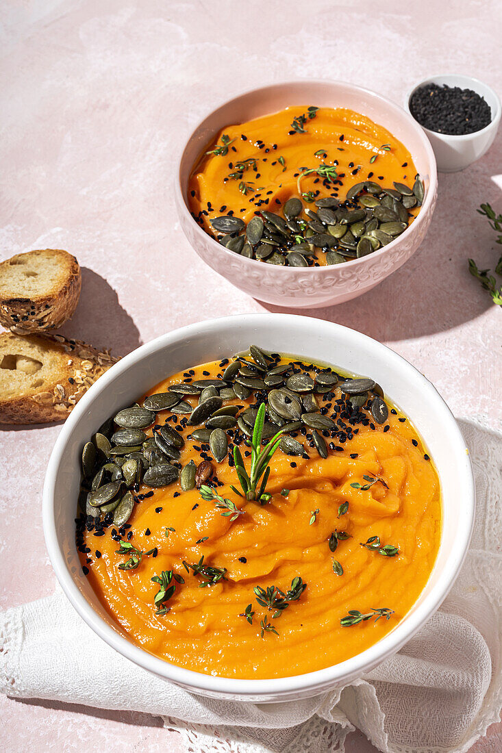 Blick von oben auf weiße Keramikschalen mit köstlicher gesunder Kürbiscremesuppe mit Kernen und Rosmarin auf dem Tisch in der Küche