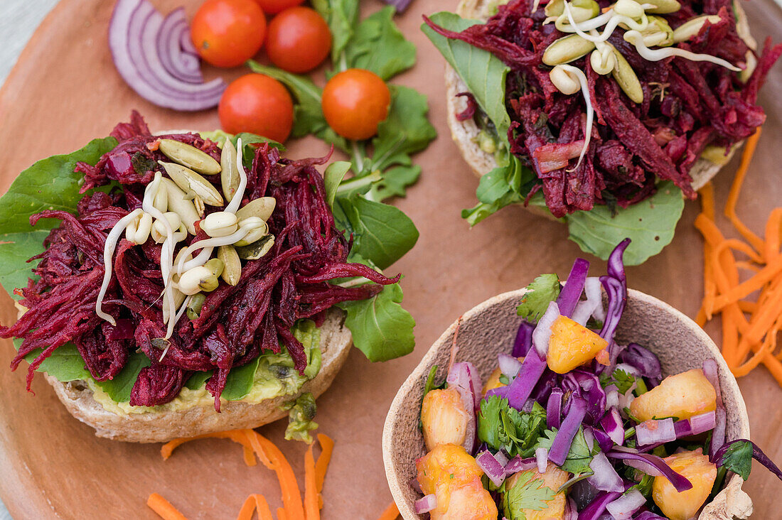 High angle of delicious sandwiches with lettuce and beetroot served with vegetables and fresh salad in bowl on wooden plate on table