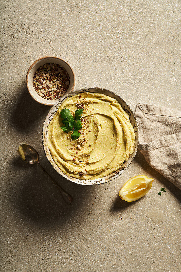 Top view bowl of delicious homemade hummus served on table with slice of lemon and chopped nuts