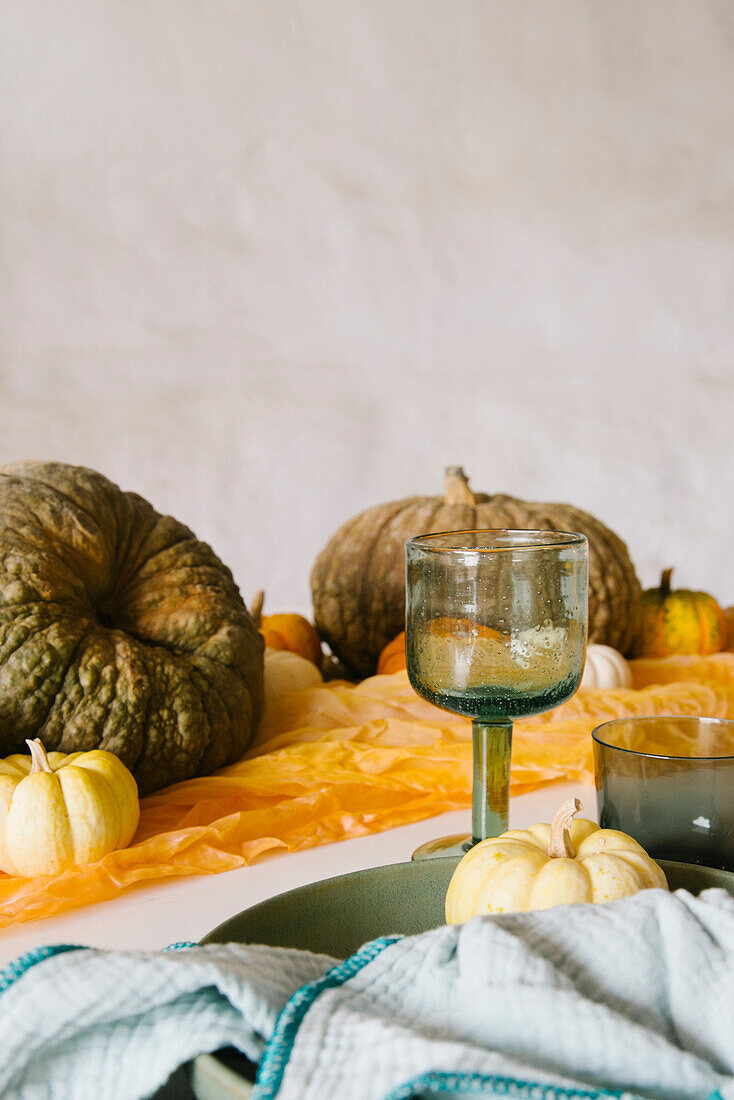 Glasses and plate with napkin served on table decorated with assorted pumpkins during Halloween celebration