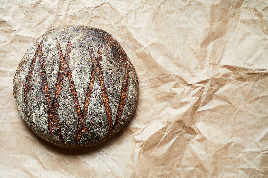 Draufsicht auf ein leckeres hausgemachtes rundes Sauerteigbrot mit knuspriger Kruste auf Pergamentpapier