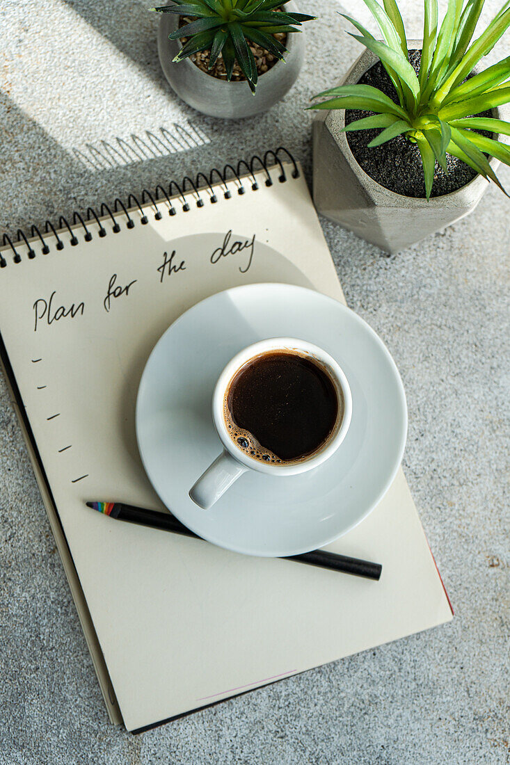 Plans for the day and morning cup of coffee on the table with green plants in the pot
