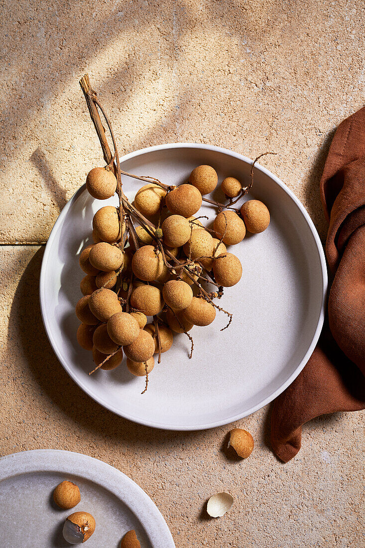 Top view of ceramic bowl with longan tropical fruit placed on tile during summer sunny day