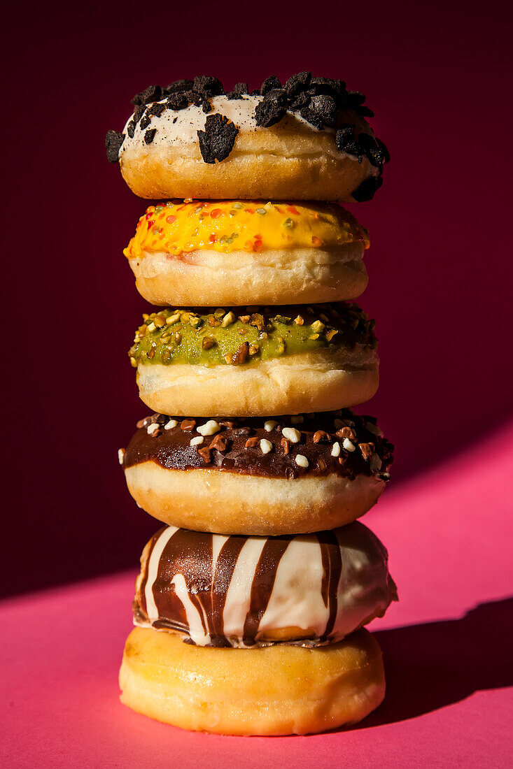Tower of donuts of different colors and flavors on pink background
