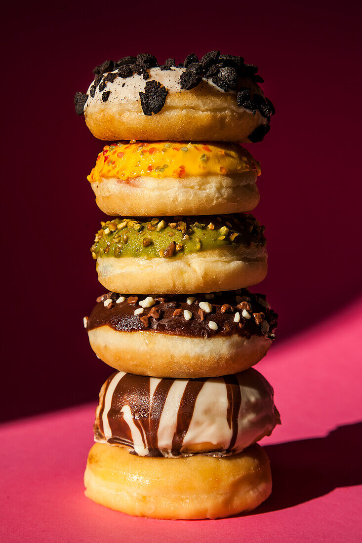 Turm von Donuts in verschiedenen Farben und Geschmacksrichtungen auf rosa Hintergrund