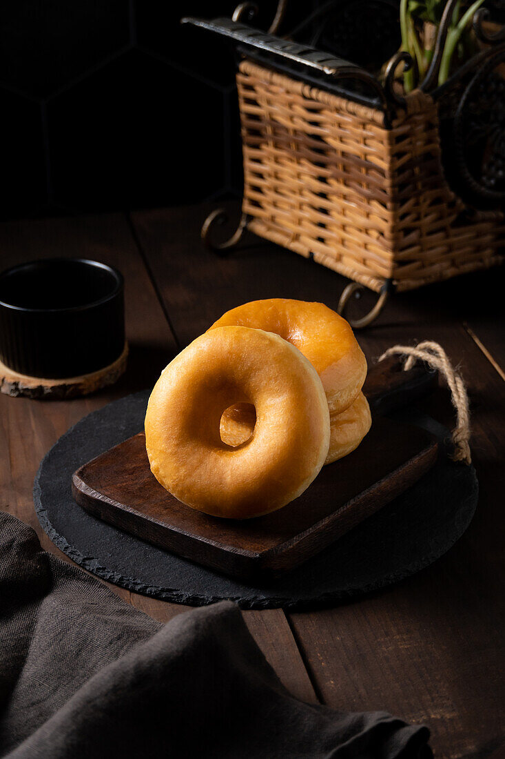 Appetitanregende, frisch gebackene Krapfen auf einem schwarzen Teller auf dem Tisch vor einem Weidenkorb