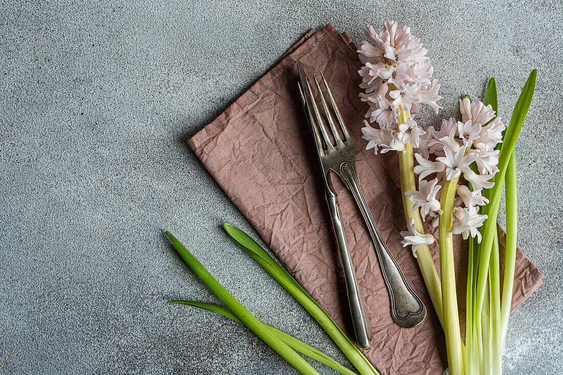 Frühlingshaft gedeckter Tisch mit Hyazinthenblüten neben Besteck auf grauem Betontisch für ein festliches Abendessen von oben