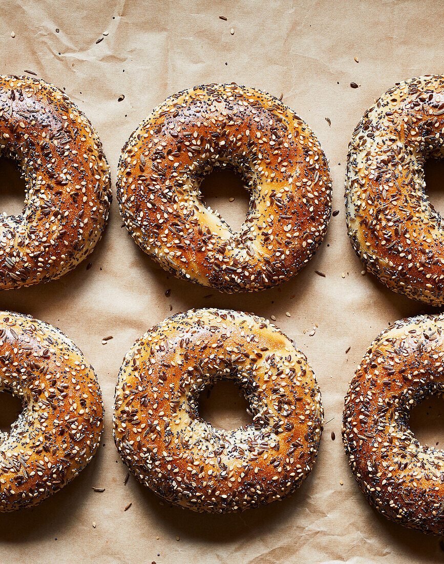 Top view of tasty baked bagels with seeds placed on parchment paper in bakery