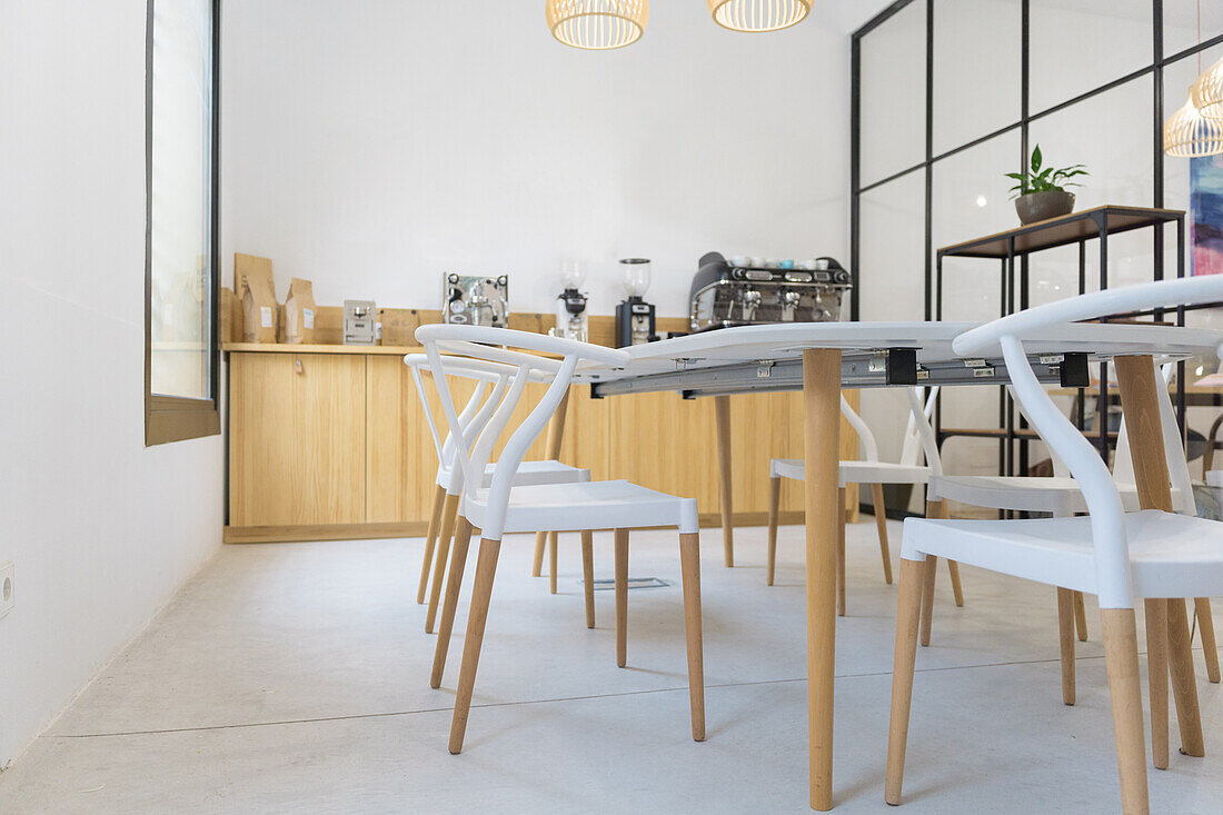 Stühle an einem Tisch neben einer Theke mit modernen Kaffeemaschinen und Kaffeemühlen auf einer Holztheke in einem geräumigen modernen Kaffeehaus