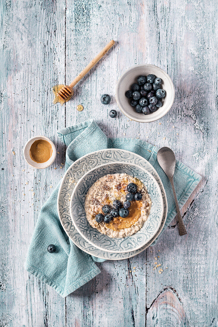 Overhead delicious fresh overnight oats porridge with blueberries and cream on kitchen towel on wooden light table