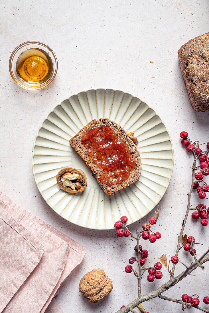 Top view of rye bread with jam near half of walnut composed with honey and branch of rowan
