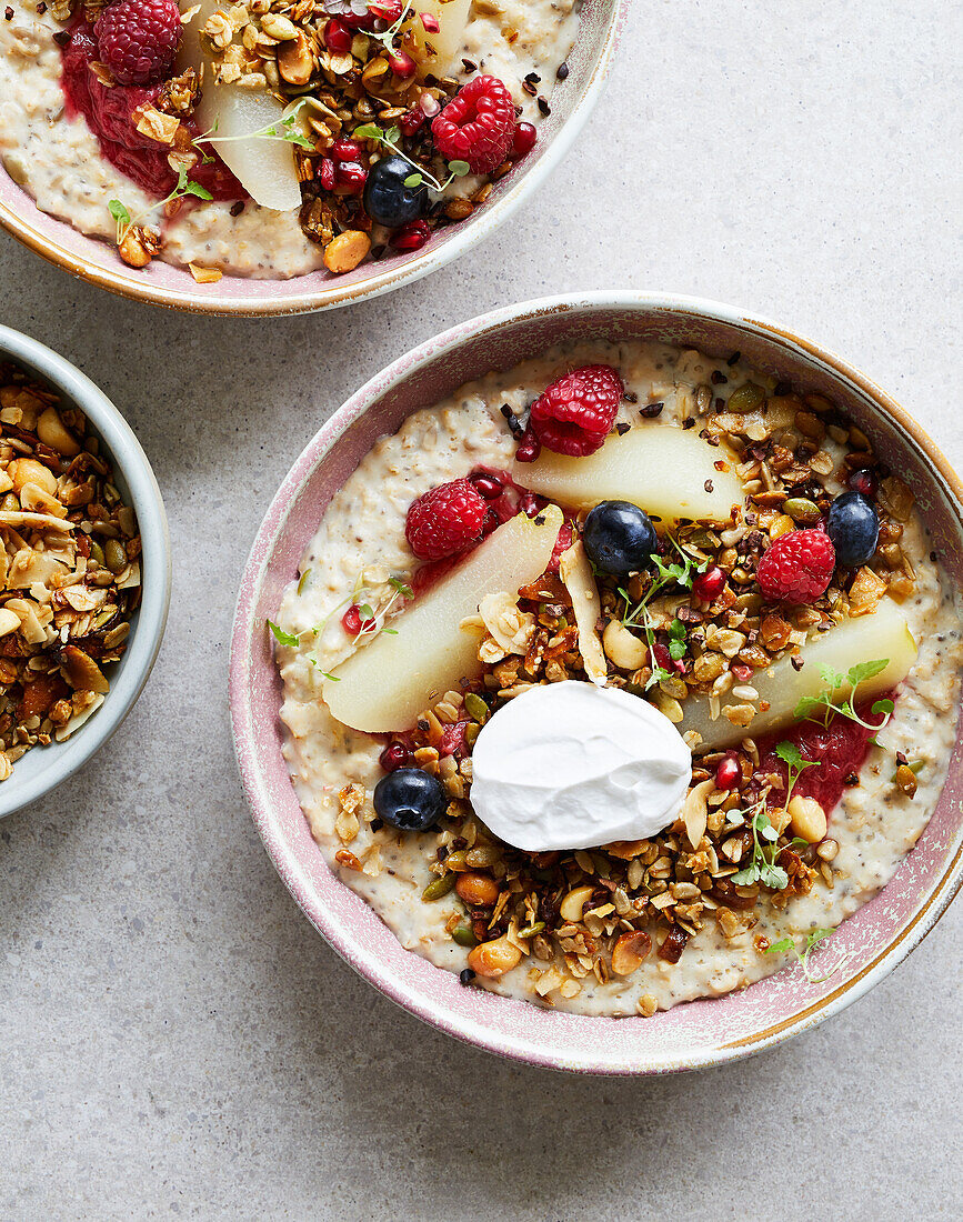 Draufsicht auf köstliche, appetitliche Haferflocken mit Blaubeeren und Himbeeren mit Müsli und Äpfeln in einer Schüssel mit Sahne serviert