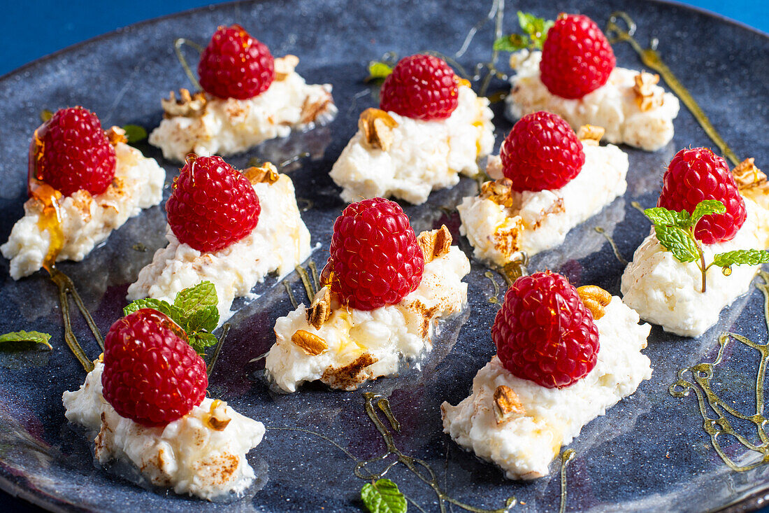 Delicious sweet dessert with cream and raspberries served with mint leaves and nuts garnished by honey on blue plate