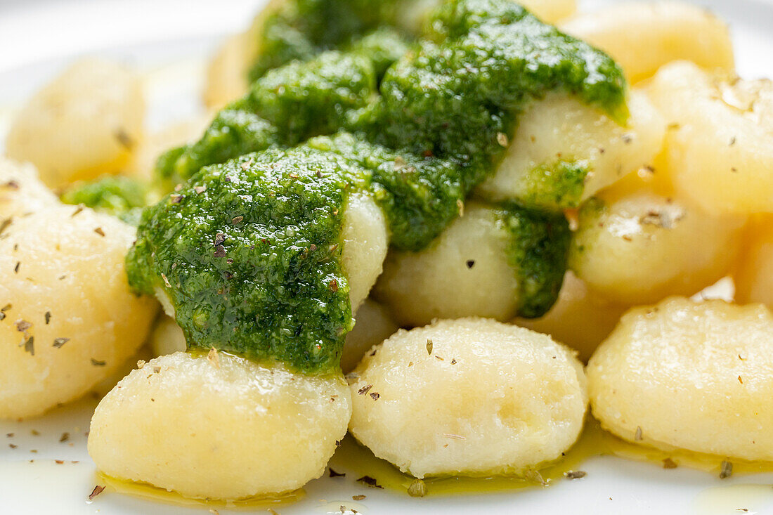 Appetizing gnocchi with pesto sauce served on white plate with toasts
