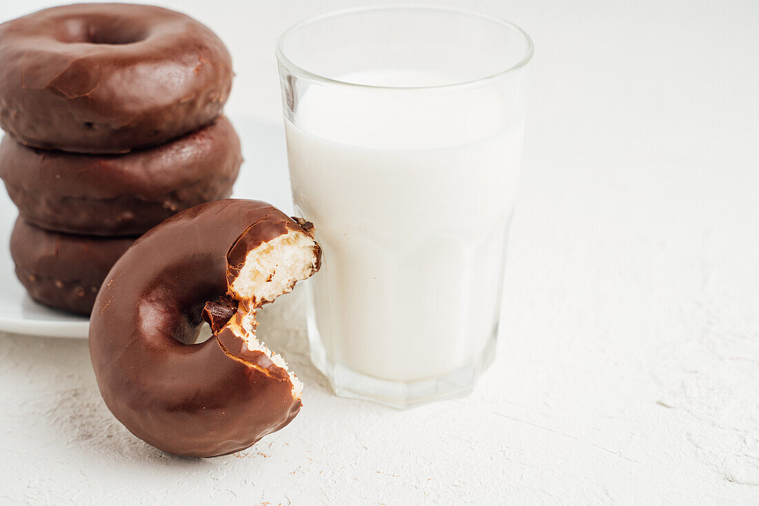 Pile of sweet tasty doughnuts with chocolate glaze placed on plate on white table with glass of milk in light room