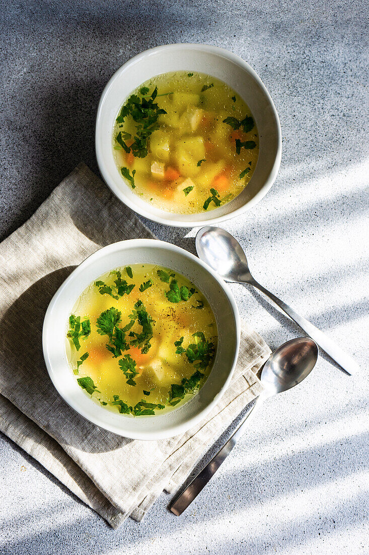 Von oben: Hühnersuppe mit Gemüse in Schalen auf weißem Betontisch, bereit zum Abendessen