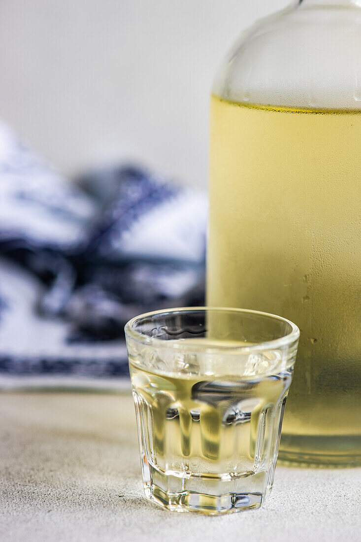 Georgian grape chacha drink in the bottle and glasses on grey concrete table with white Supra tablecloth