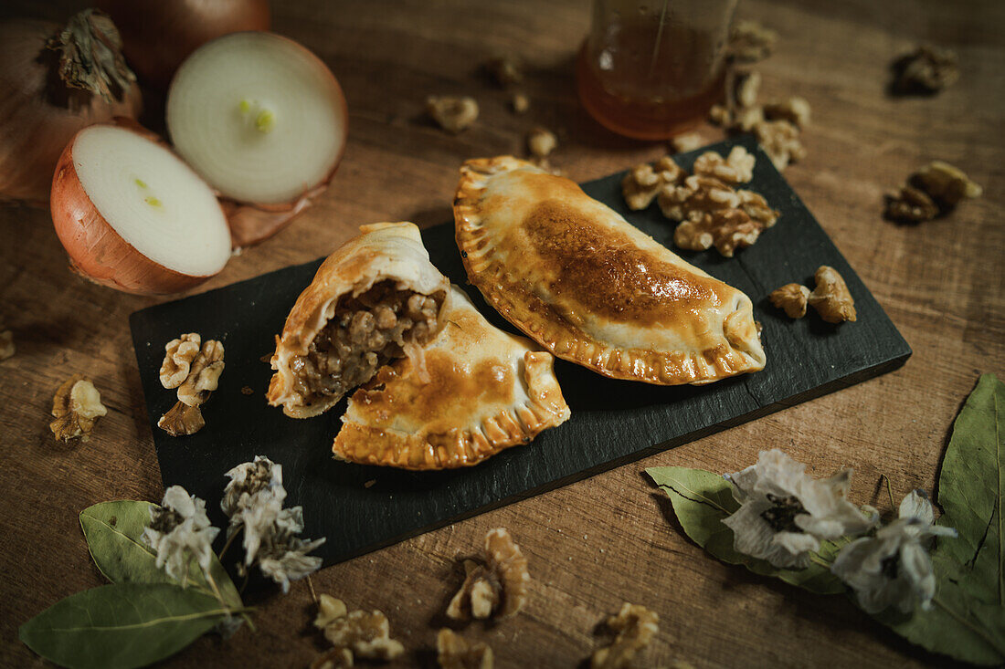 Appetitliche argentinische Empanadas, die auf einem flachen Teller auf einem Holztisch in der Nähe von Zutaten in der Küche serviert werden, von oben