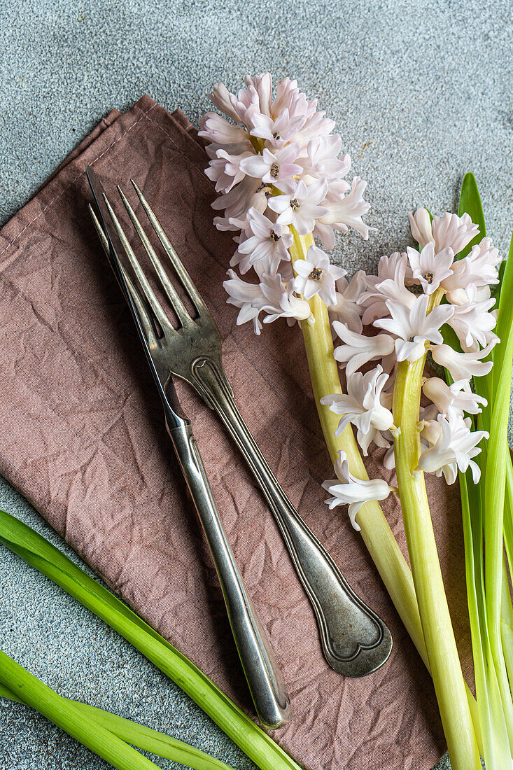 Frühlingshaft gedeckter Tisch mit Hyazinthenblüten neben Besteck auf grauem Betontisch für ein festliches Abendessen von oben
