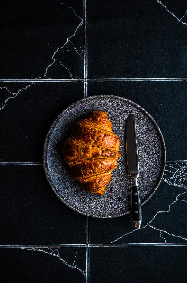 Von oben frisch gebackenes Croissant mit Marmelade auf dem gefliesten schwarzen Betontisch