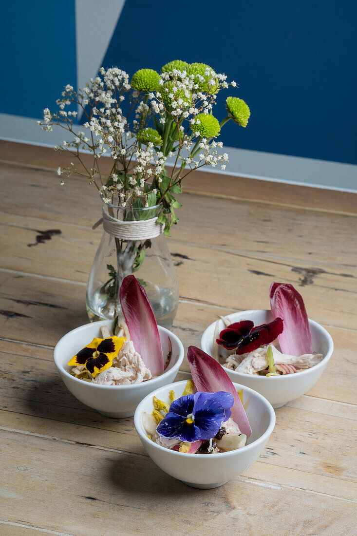 Von oben frisch zubereitete Desserts, dekoriert mit hellen, blühenden Blumen und serviert in Keramikschalen neben Schleierkraut in Glasvase