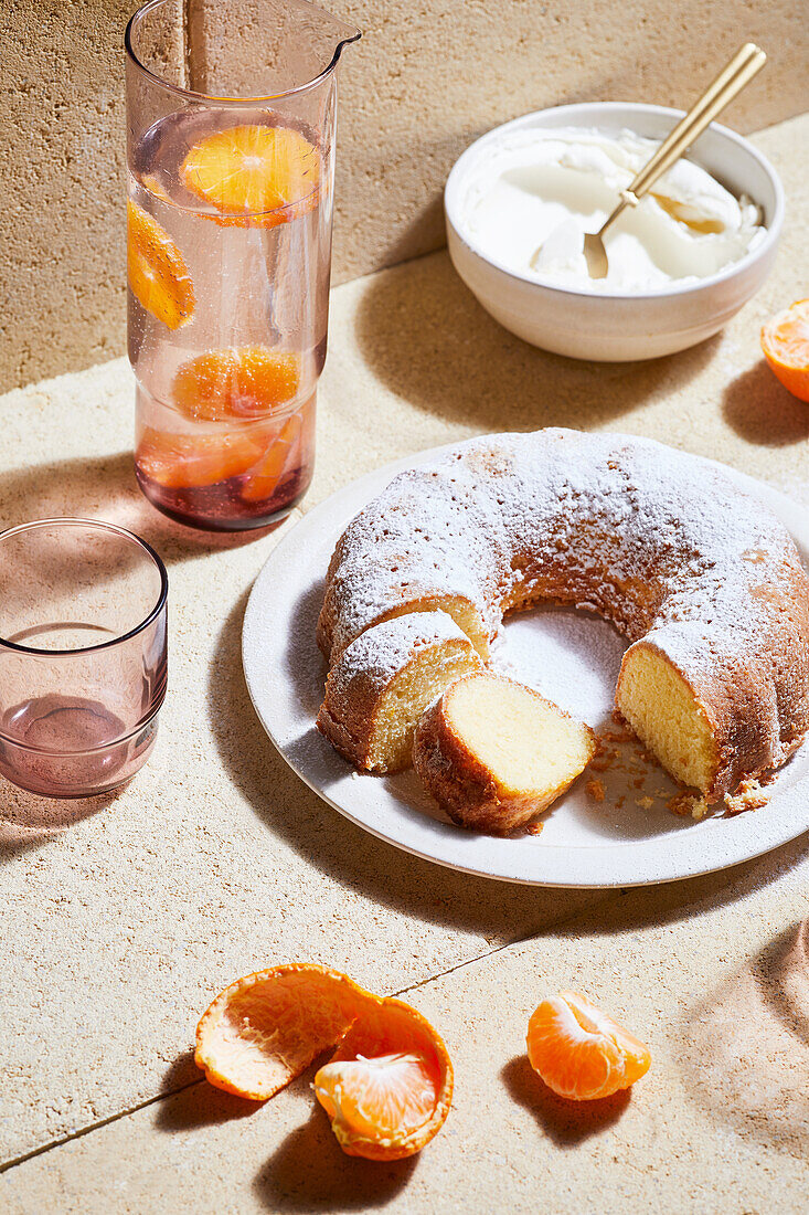 High angle of appetizing sweet cake sprinkled with sugar powder placed near mandarin lemonade