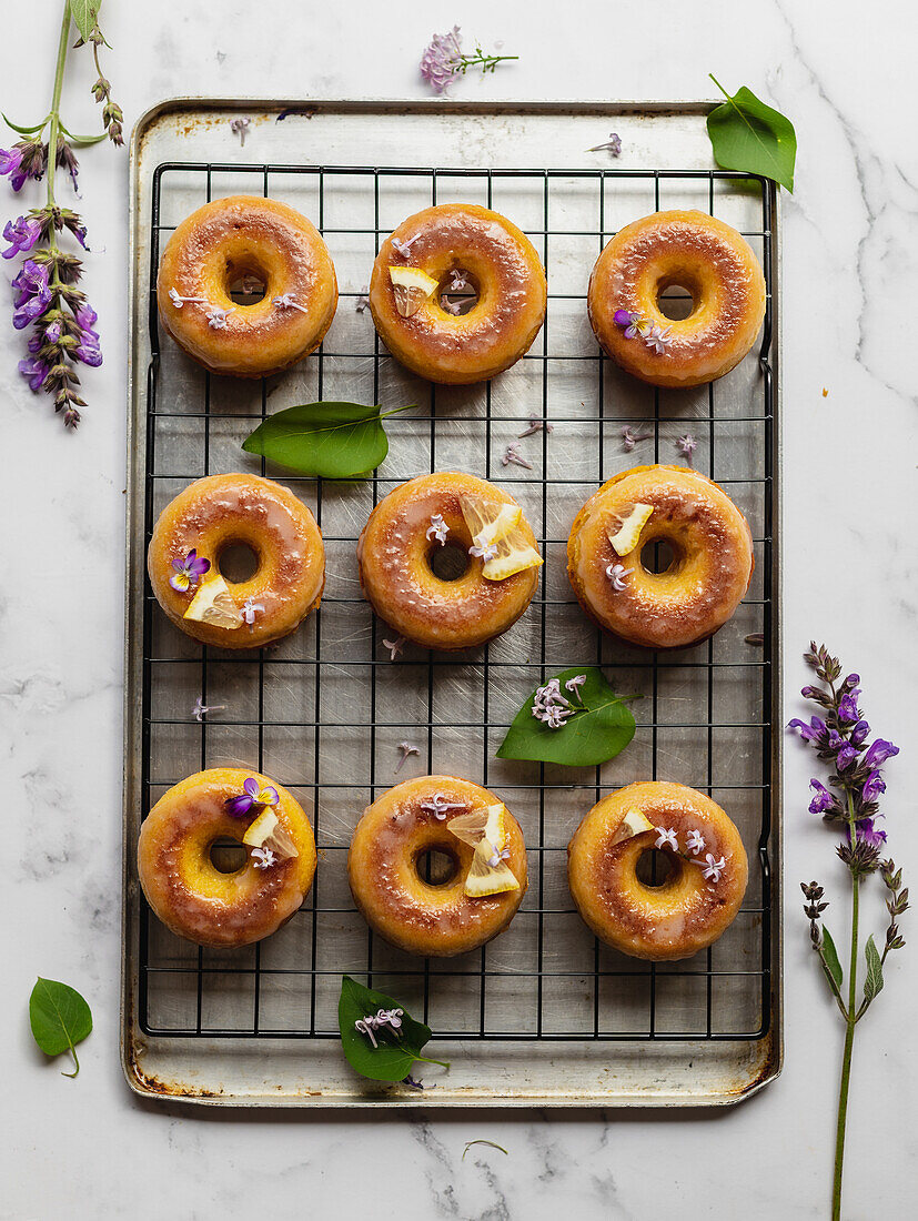 Top view of tasty donuts on cooling rack with leaves between blooming lavender sprigs on marble surface