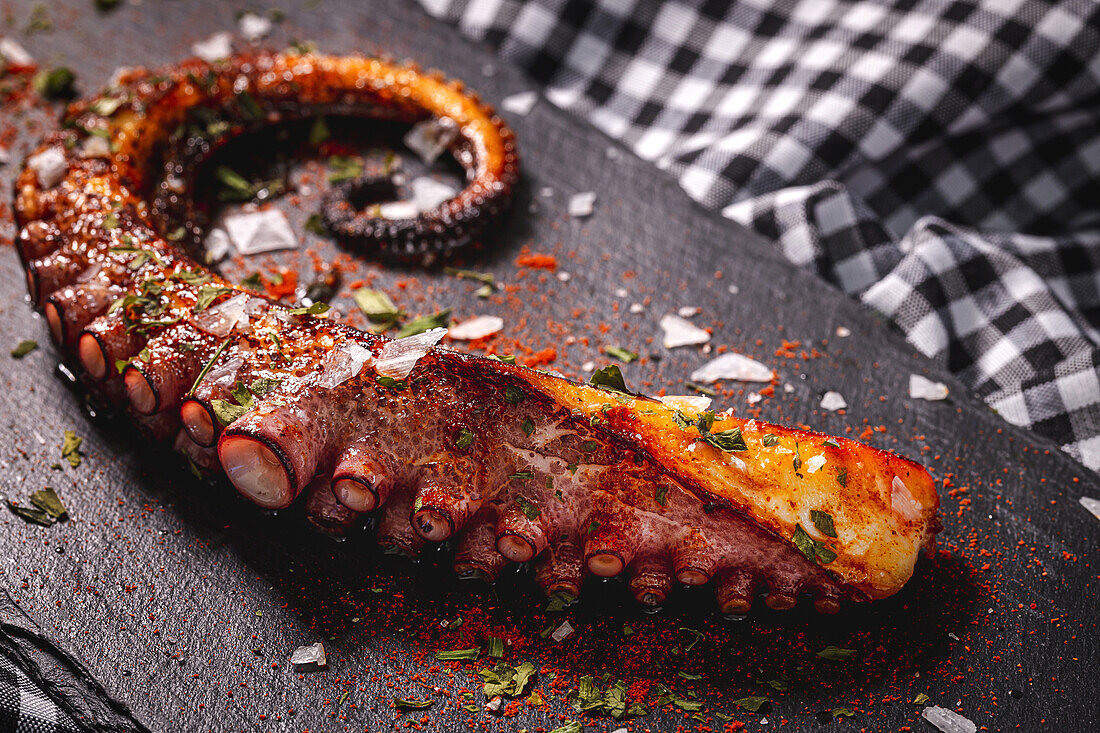 From above delicious grilled octopus tentacle served with spices on wooden board on checkered cloth