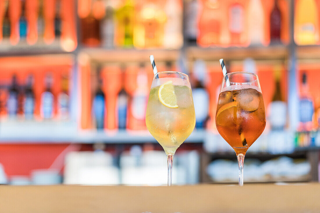 Glasses of cold fresh cocktails served on glass with straw on wooden counter in bar