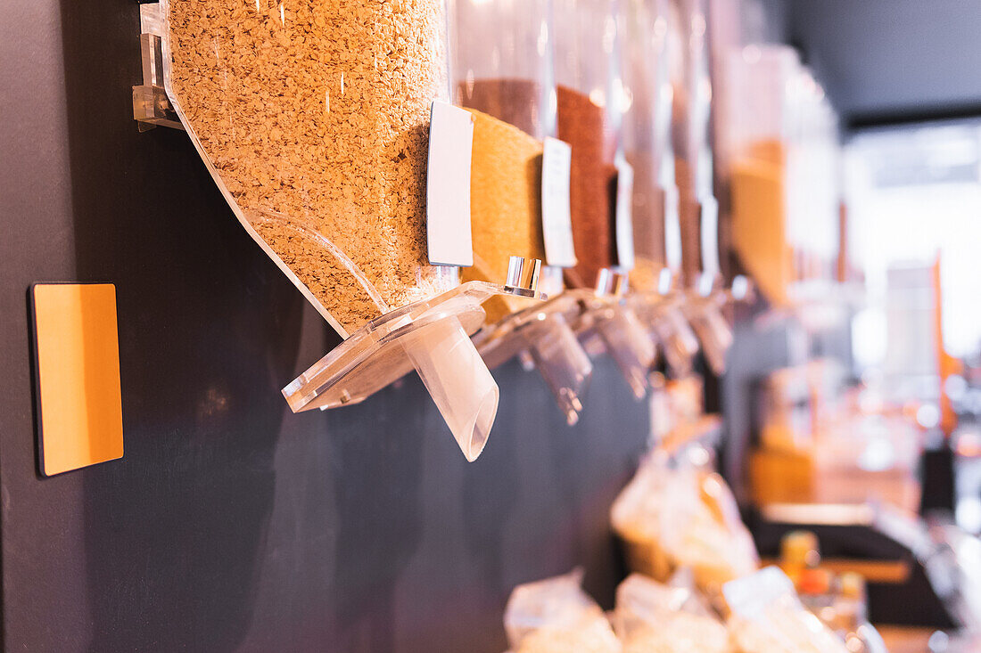 Plastic dispensers with assorted grains hanging on wall in eco friendly grocery store