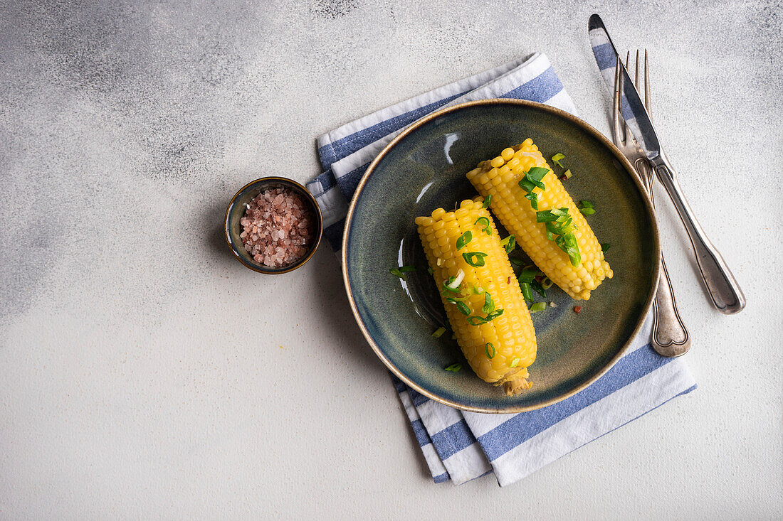 Top view of boiled corn with salt and green onion served on plate on grey background