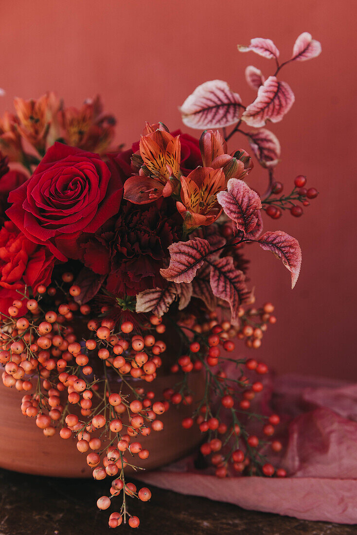 Ausschnitt eines eleganten Blumenstraußes aus frischen, üppigen roten Rosen und Lilien mit Zweigen roter Beeren, die in der Nähe des Stoffes platziert sind