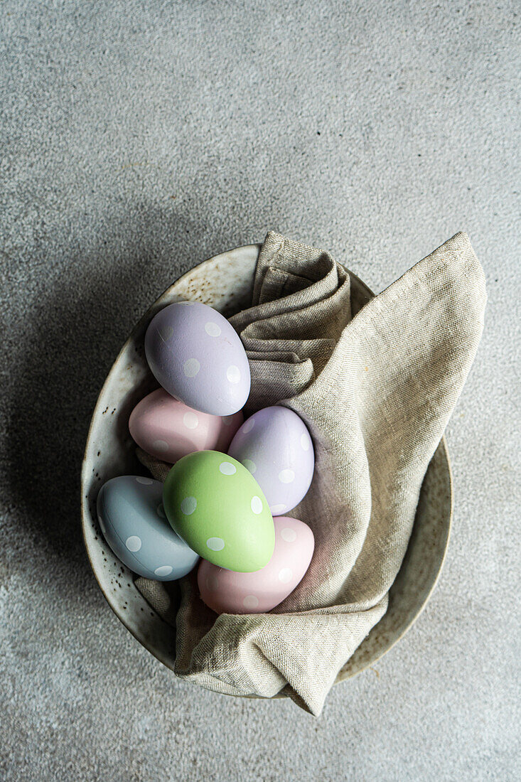 Von oben auf einen grauen Betontisch mit bunten Eiern auf einer Keramikschale für ein festliches Abendessen