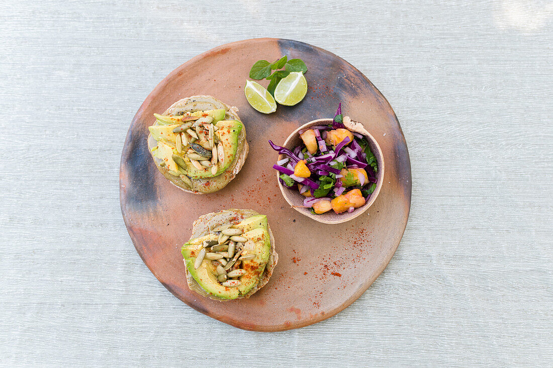 Overhead view of plate with bowl of vegetable salad and sandwiches with pate garnished with avocado slices and pumpkin seeds served on table for healthy lunch