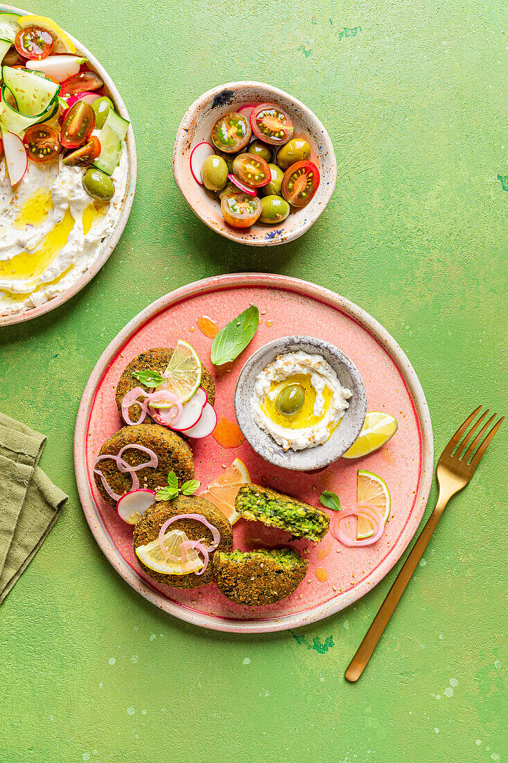 Top view of plate with delicious cream cheese and assorted vegetables placed on napkin near vegan fritters on green background