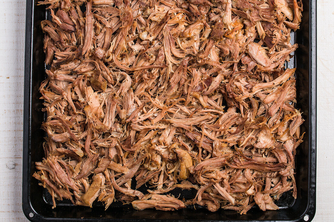 Top view of pile of cooked pulled meat on small fibers and pieces covering baking pan while preparing Cuban bowl
