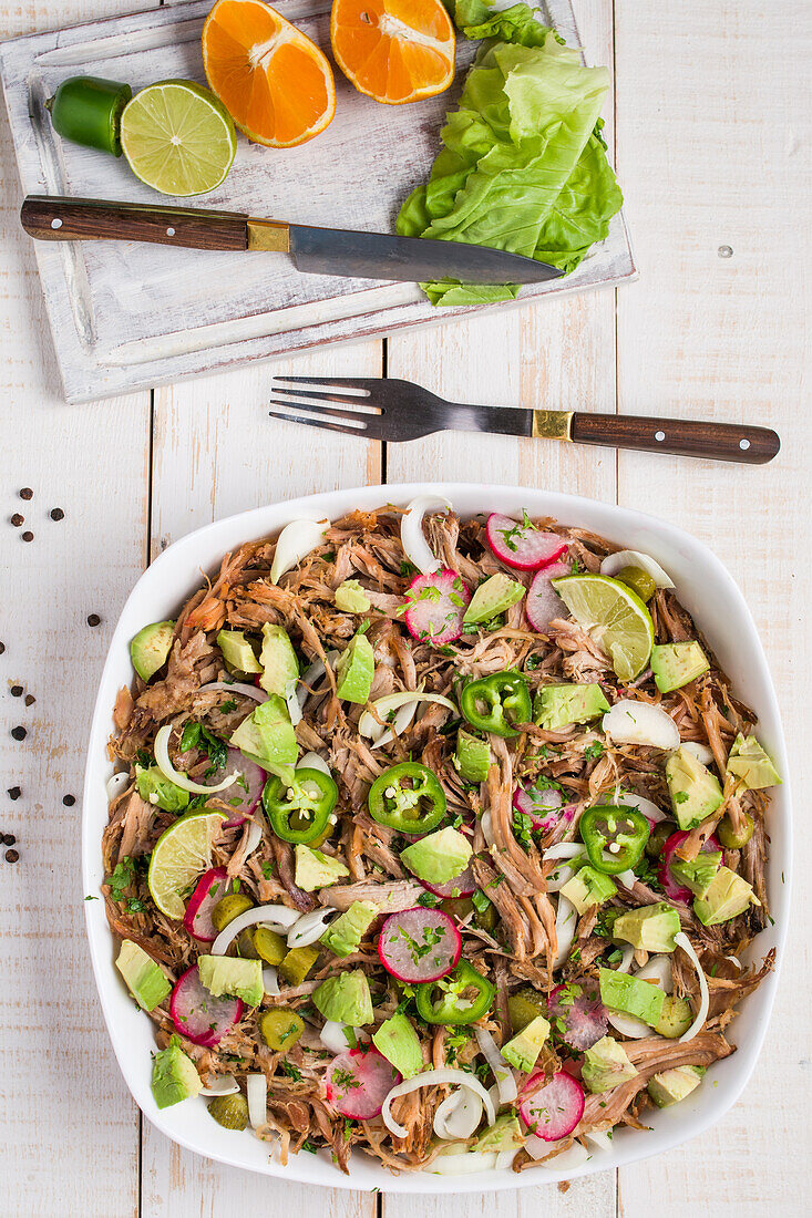 Top view of Cuban bowl with pulled meat and chopped avocado with jalapeno and radish and lime served in white ceramic bowl