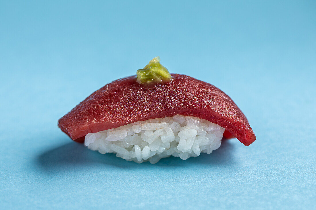 Traditionelle japanische köstliche Blauflossen-Nigiri mit Reis und frischem Thunfisch mit würzigem Wasabi vor blauem Hintergrund im hellen Studio serviert