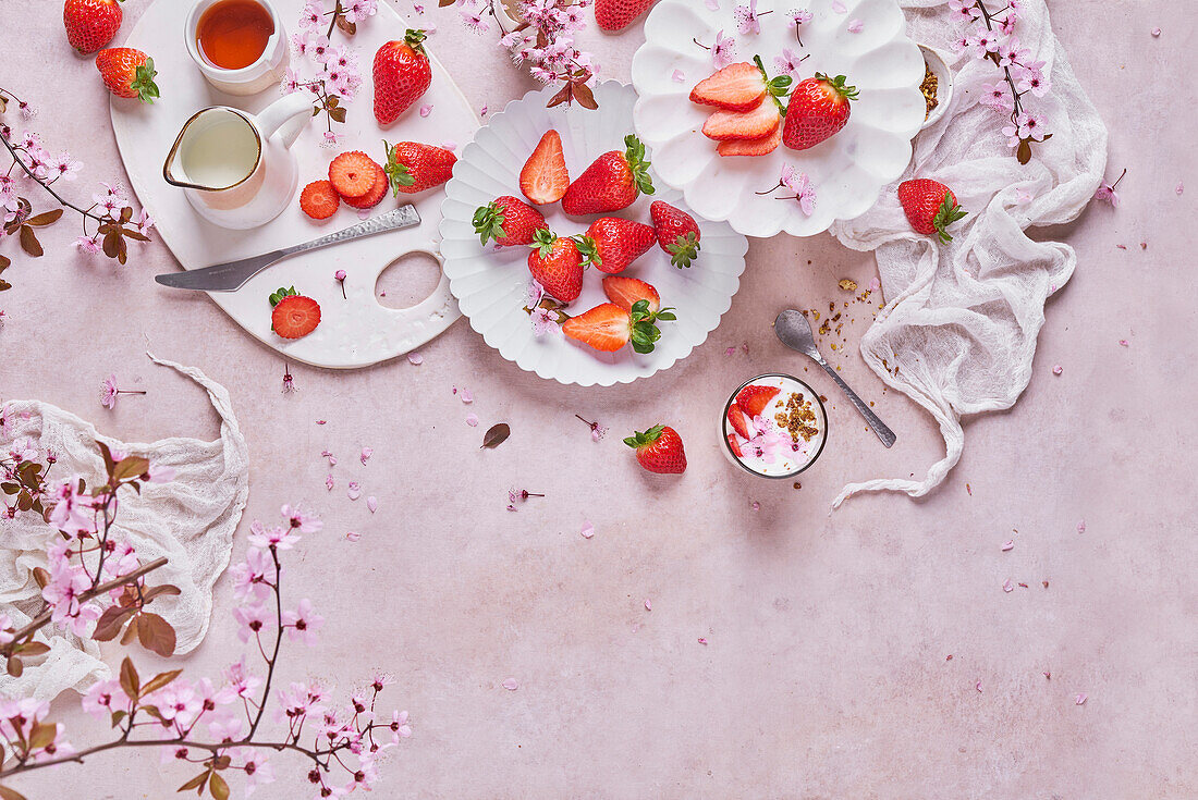 Blick von oben auf ein Glas köstlichen Joghurts mit Müsli auf einem Tisch neben Tellern mit frischen reifen Erdbeeren, die auf einem Tisch in der Küche serviert werden