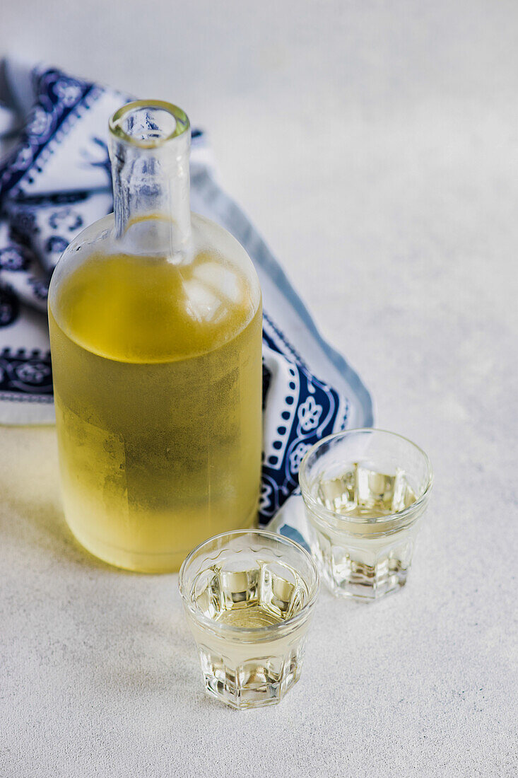 Georgisches Traubentschacha-Getränk in der Flasche und Gläser auf grauem Betontisch mit weißer Supra-Tischdecke