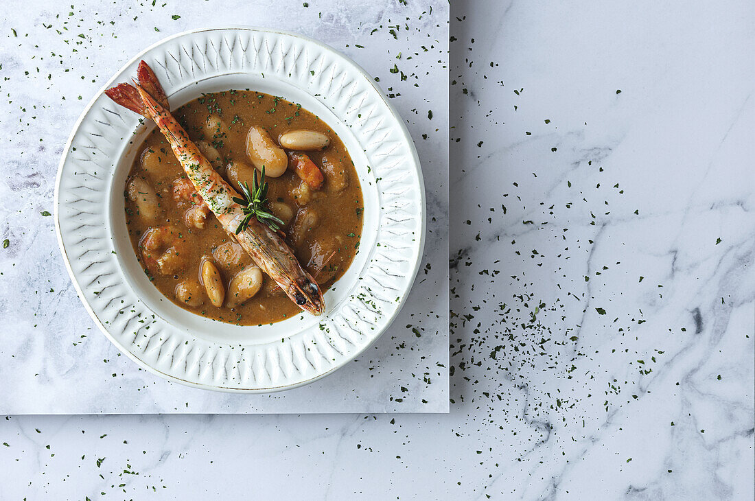 From above of appetizing cream soup with white beans and langoustines served in bowl and placed on marble tabletop in kitchen