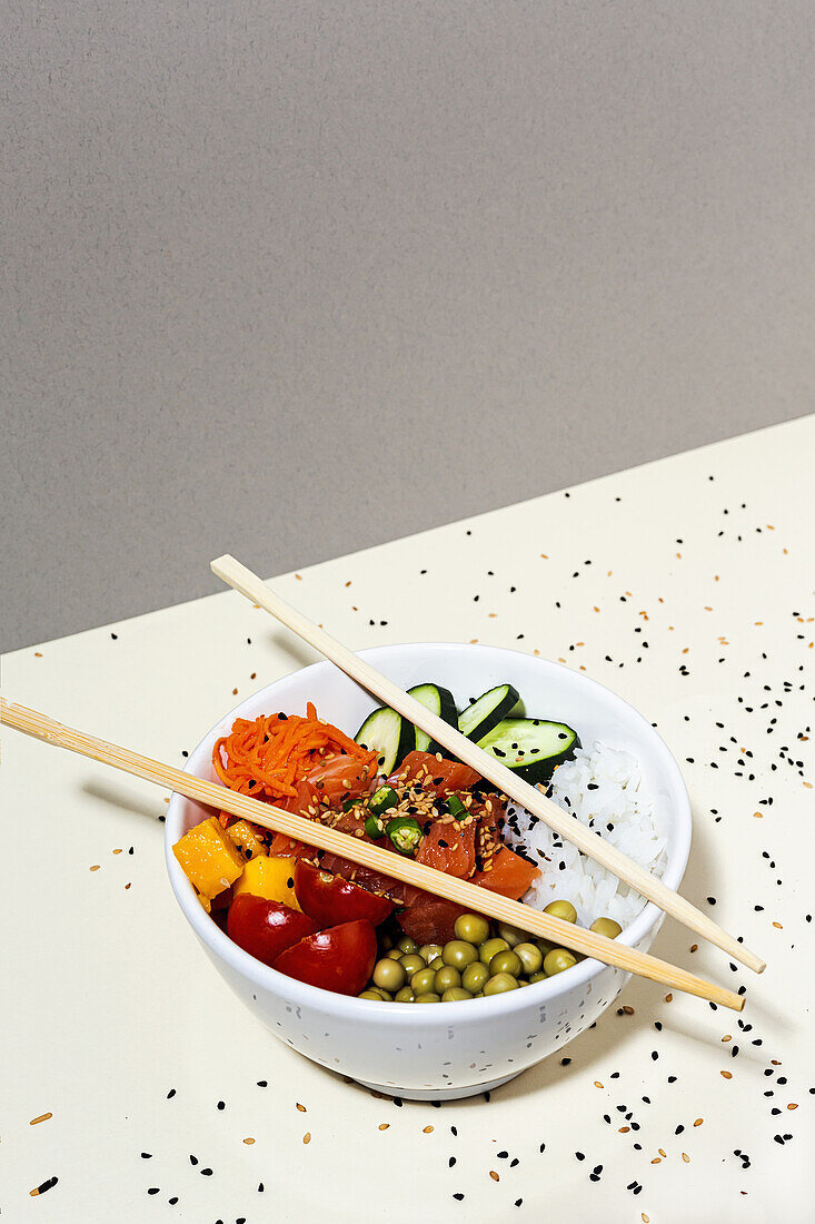 Von oben Bambus-Essstäbchen auf Schüssel mit leckerem Poke-Gericht auf Tisch mit Sesamsamen bedeckt platziert