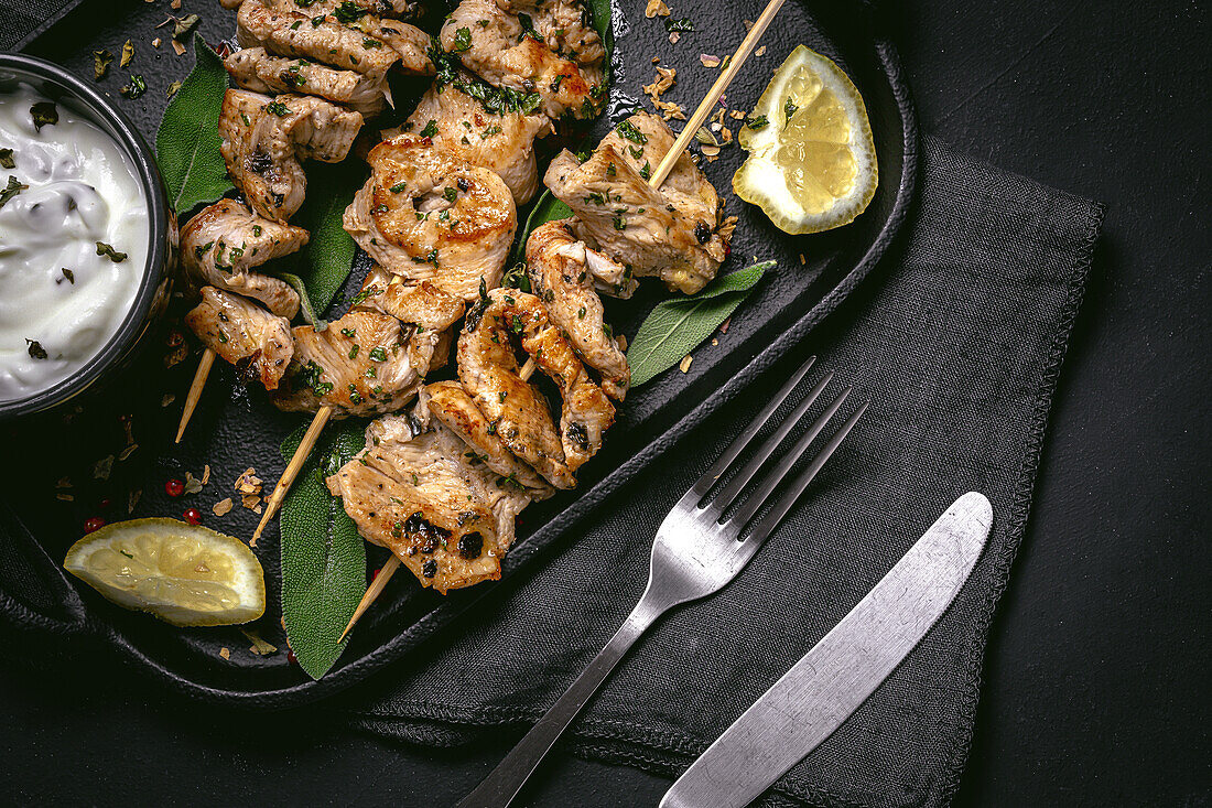 Appetitliches, frisch zubereitetes Fleisch am Spieß, serviert auf einem Tablett auf einem schwarzen Tisch mit einer Schale mit Soße