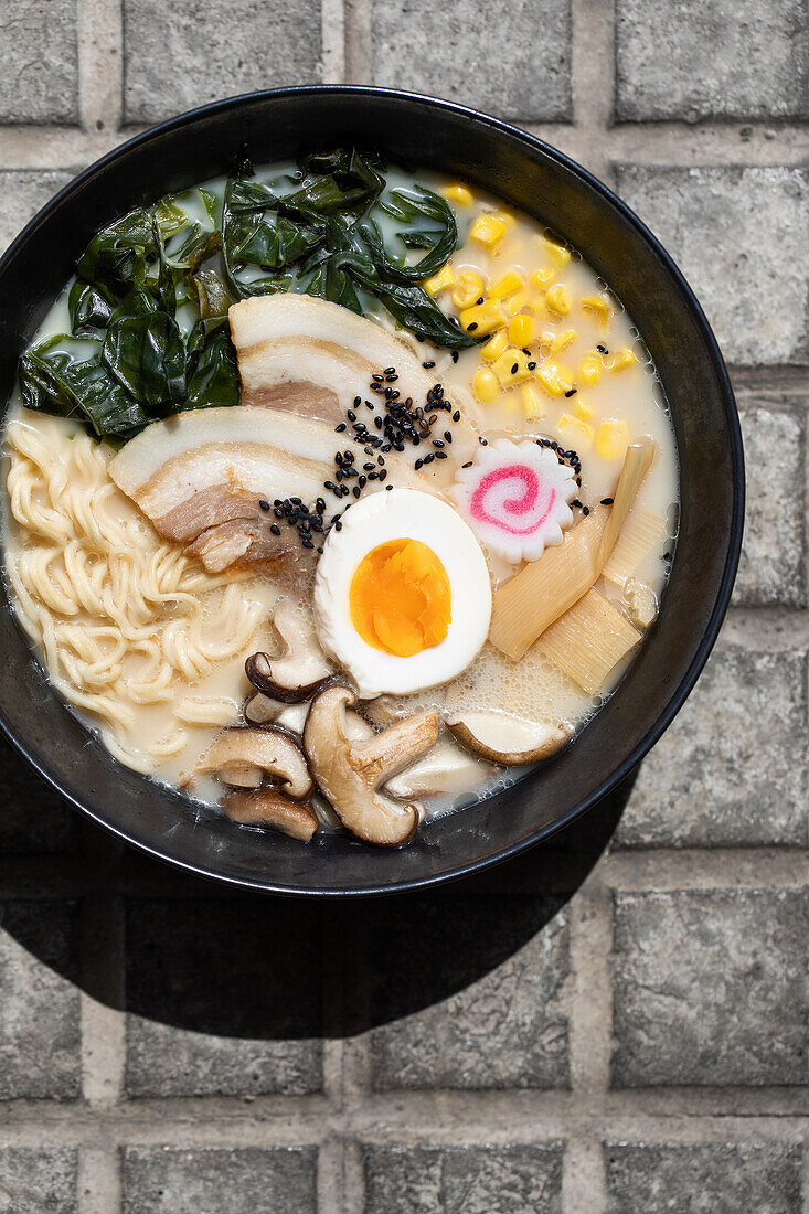 Top view of appetizing Japanese ramen with mushrooms and egg served on paved sidewalk on sunny street in city